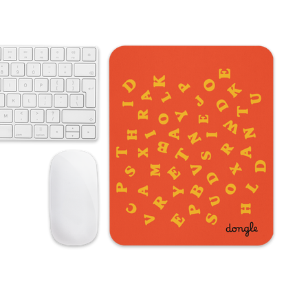 Orange mousepad with scattered yellow alphabet letters and a white wireless mouse on top, designed by Dongle