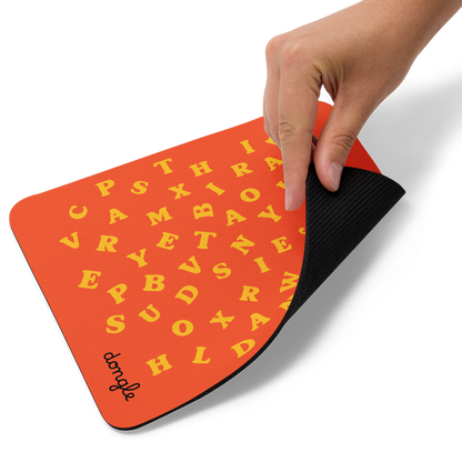 Orange mousepad with scattered yellow alphabet letters and a white wireless mouse on top, designed by Dongle